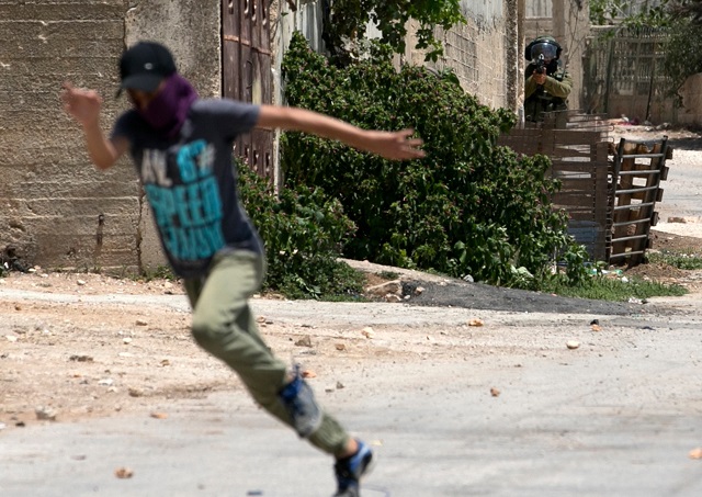 a palestinian protester runs away from an aiming israeli soldier during clashes with israeli forces following a weekly demonstration against the expropriation of palestinian land by israel in the village of kfar qaddum near nablus in the occupied west bank on july 20 2018 photo afp