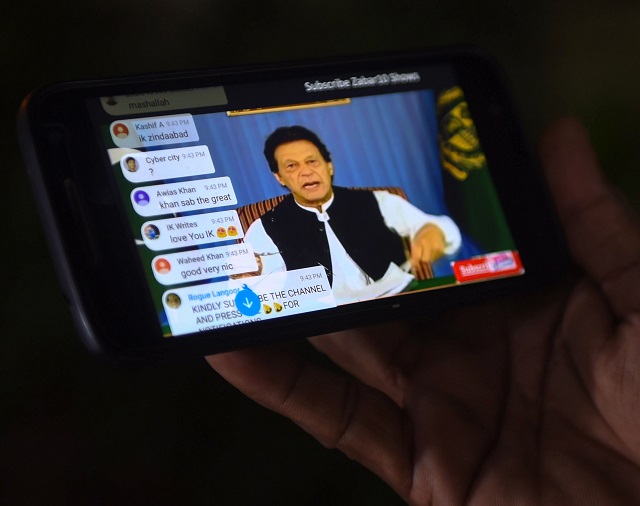 a man holds his smartphone as he watches a broadcast of a speech of newly appointed prime minister imran khan as he addresses the nation in karachi on august 19 2018 photo afp