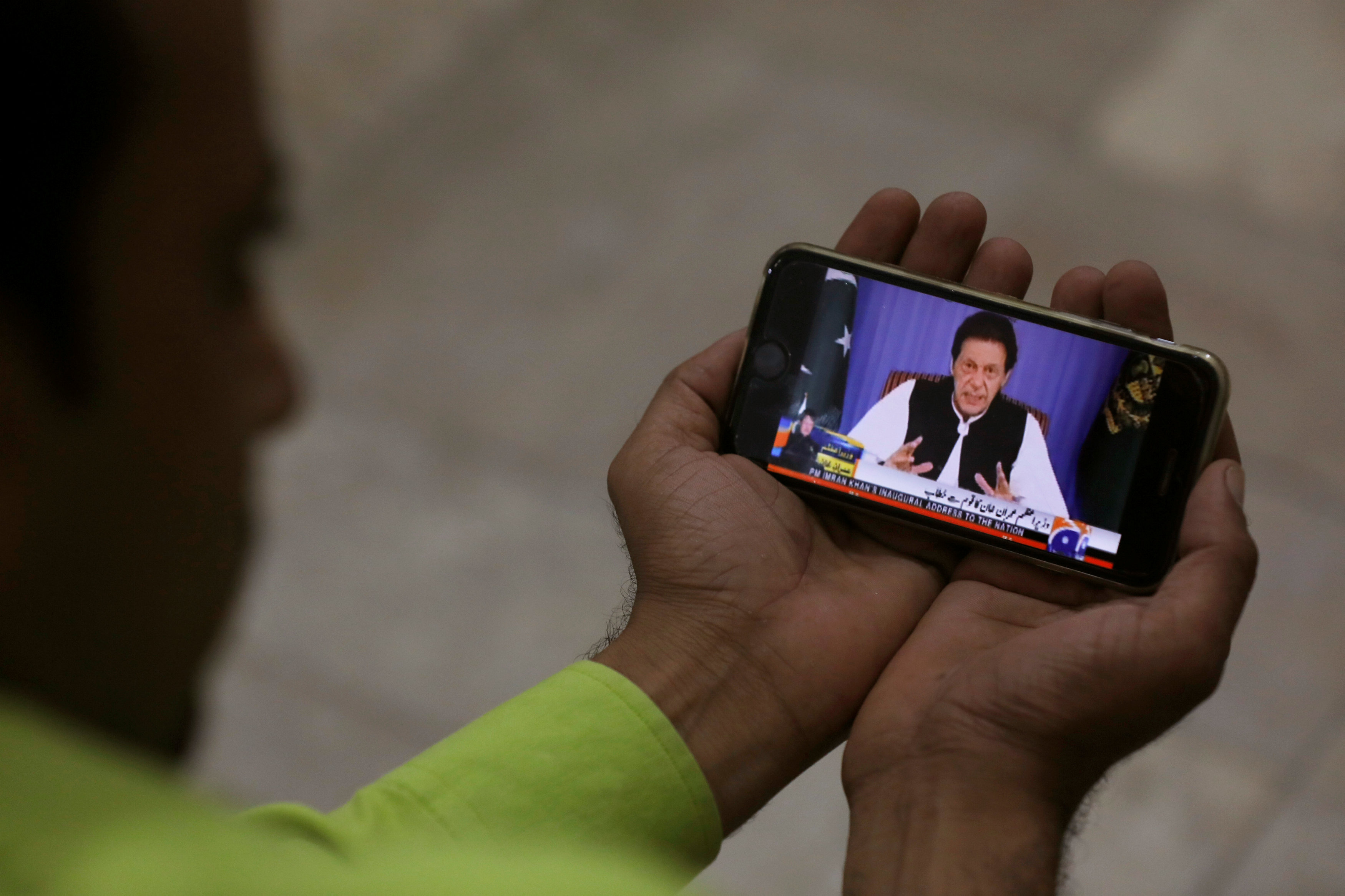 a man poses with a cell phone displaying pm imran speaking to the nation in his first televised address photo reuters