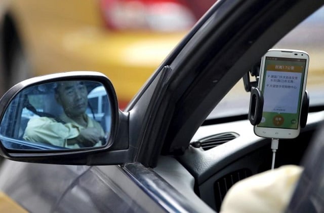 a taxi driver is reflected in a side mirror as he uses the didi chuxing car hailing application in beijing china september 22 2015 photo reuters