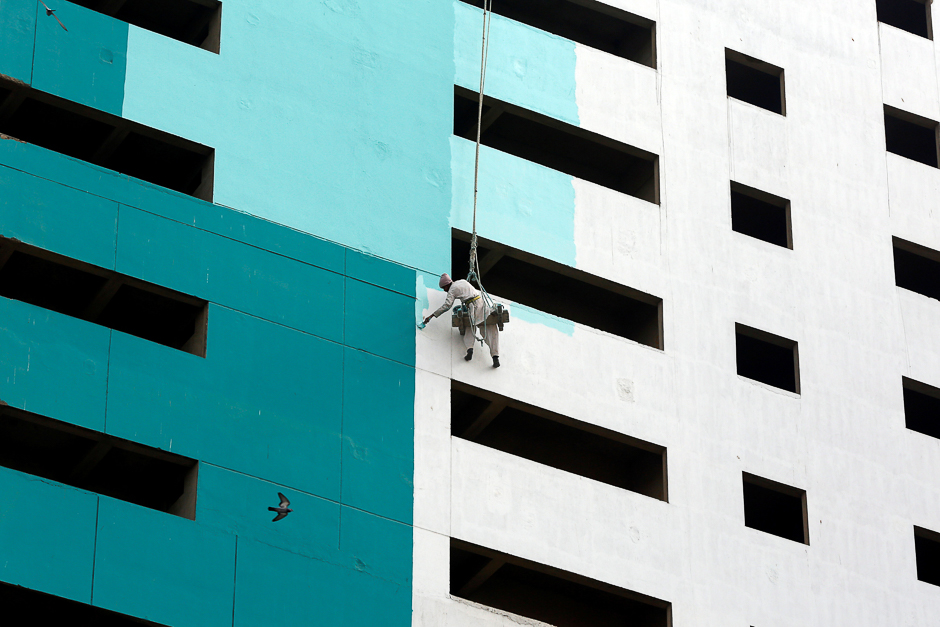 A bird flies past a labourer, suspended with a rope, as he paints a newly constructed building in Karachi. PHOTO: REUTERS