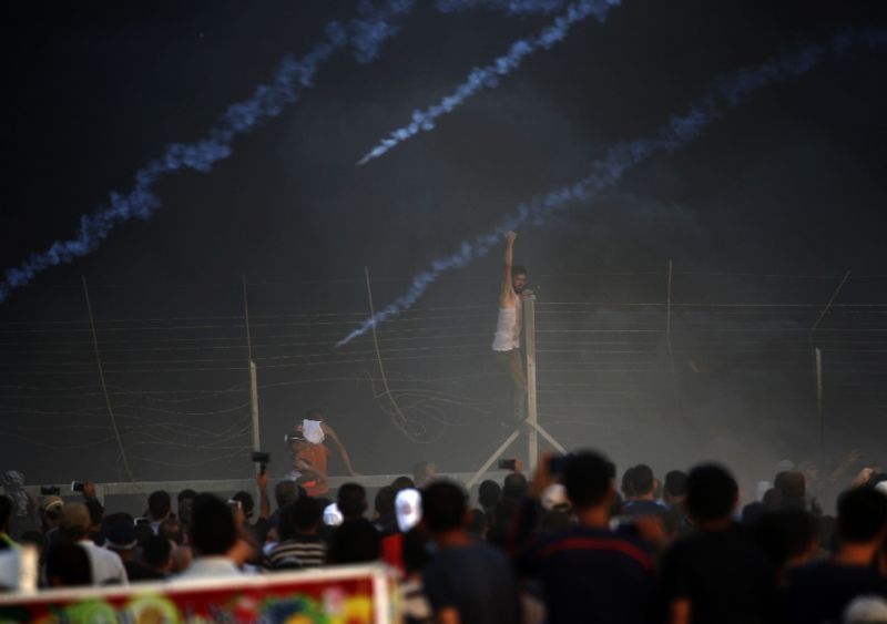 a palestinian protester climbs a fence in gaza as tyres burn and israeli forces fire tear gas canisters during a demonstration along the frontier with israel east of gaza city photo afp