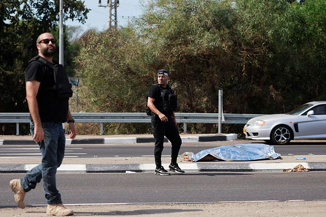 Israeli security personnel walk near the body of a dead man, as Hamas launches a surprise attack from the Gaza Strip, near Ashkelon, southern Israel October 7, 2023. REUTERS