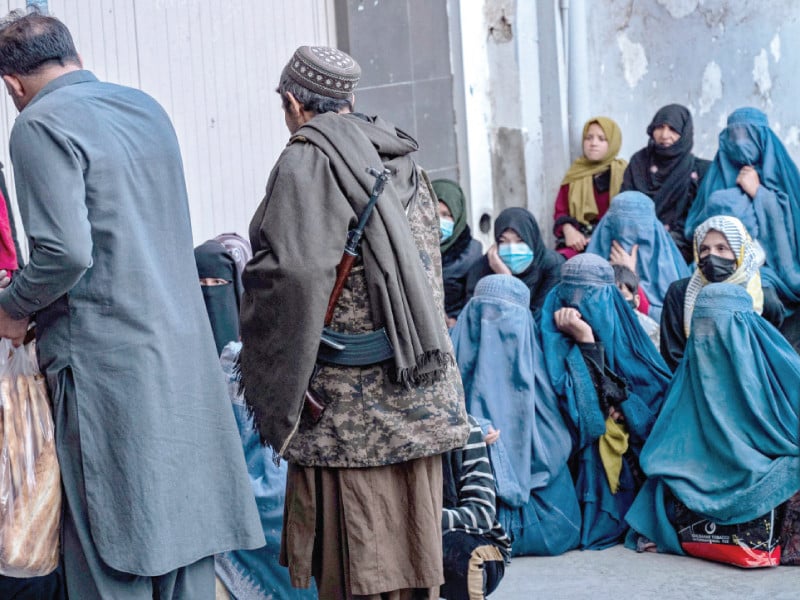 a taliban security personnel stands guard as afghan burqa clad women wait to receive free iftar meals in kabul photo afp