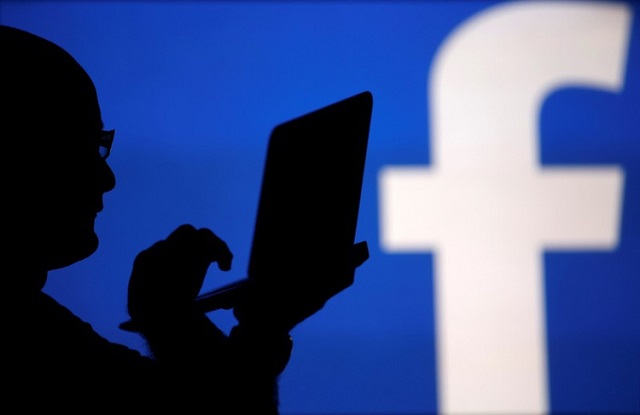 a man is silhouetted against a video screen with an facebook logo as he poses with a laptop in this photo illustration photo reuters