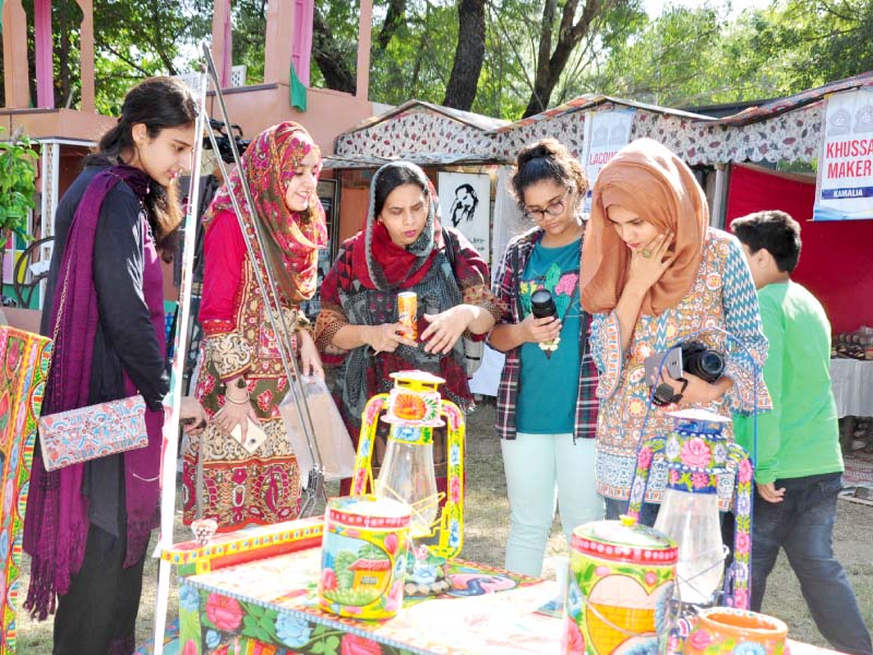 women look at items on display while schoolgirls enjoy a folk song at lok mela on monday photos express