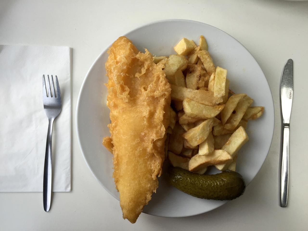 a plate of traditional fish and chips with a gherkin on a table in a seafront fish and chip shop in brighton britain photo reuters