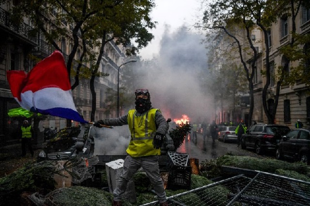 a protester waves the french flag over a barricade made of christmas trees during the quot yellow vest quot protests in paris on saturday   photo afp
