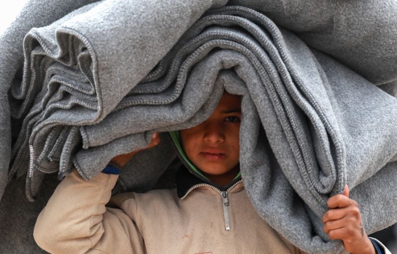 a syrian displaced boy carries blankets over his head inside the internallly displaced persons idp camp of al hol in northeast syria photo afp