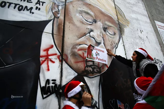 palestinians dressed as santa claus hang signs on a mural painting of us president donald trump on israel 039 s controversial separation barrier in the west bank city of bethlehem on december 23 2018 photo afp
