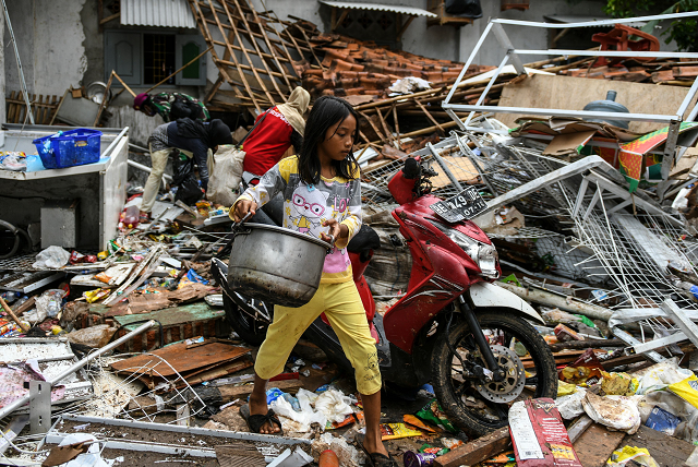 a girl carries her belongings from her collapsed home in rajabasa in lampung province photo afp