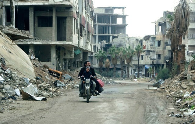 a syrian man drives past destrpoyed buildings in arbin on december 18 2018 photo afp