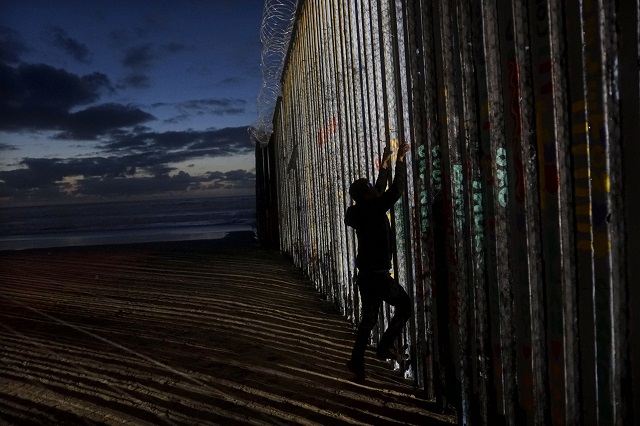 a man prepares to climb on the u s  mexico border wall on january 6 2019 in tijuana mexico photo afp