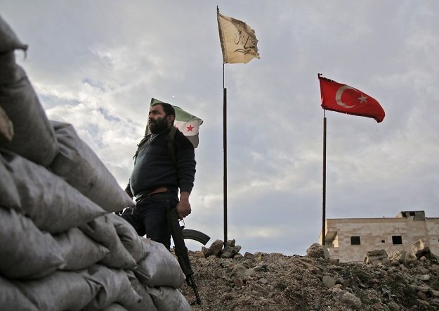 a fighter from faylaq al sham sham or levant legion one of the factions of the turkish backed national liberation front nlf factions is seen holding a kalashnikov assault rifle as he stands in front of the flags of l to r the syrian opposition the faction and turkey at a position in the village of kiridiyah about 30 kilometres west of the northern town of manbij photo afp