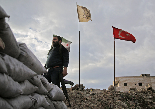 a fighter from faylaq al sham sham or levant legion one of the factions of the turkish backed national liberation front nlf factions is seen holding a kalashnikov assault rifle as he stands in front of the flags of l to r the syrian opposition the faction and turkey at a position in the village of kiridiyah about 30 kilometres west of the northern town of manbij on january 15 2019 photo afp