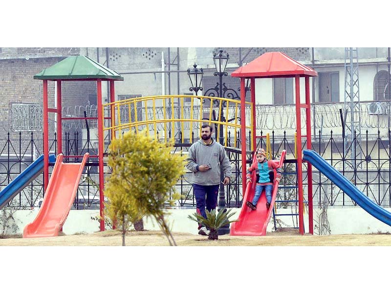 a man stands by as a child enjoys herself on a slide in shehbaz sharif park in rawalpindi photo app