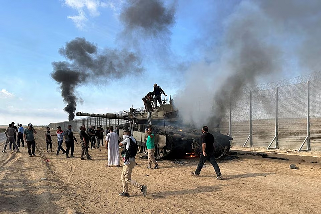 Palestinians react as an Israeli military vehicle burns after it was hit by Palestinian gunmen who infiltrated areas of southern Israel, at the Israeli side of Israel-Gaza border, October 7, 2023. REUTERS