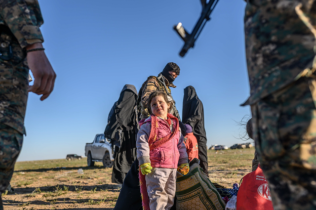 a toddler looks at members of the kurdish led syrian democratic forces sdf while awaiting to be searched after leaving the islamic state is group 039 s last holdout of baghouz in the eastern syrian deir ezzor province on march 1 2019 photo afp