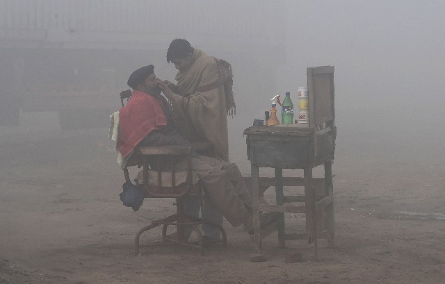 files in this file photo taken on january 24 2019 a pakistani barber shaves a customer alongside a road amid heavy fog and smog conditions in lahore photo afp