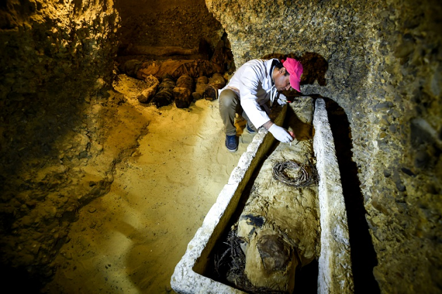 an archaeologist brushes a newly discovered mummy laid inside a sarcophagus part of a collection found in burial chambers dating to the ptolemaic era 323 30 bc in february 2019 photo afp