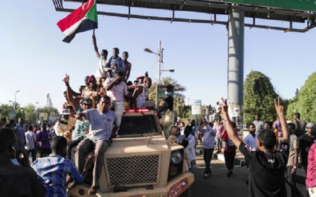 sudanese protesters wave a national flag and flash the victory sign as they sit atop a military vehicle next to soldiers near the capital khartoum 039 s military headquarters on 7 april 2019 photo afp