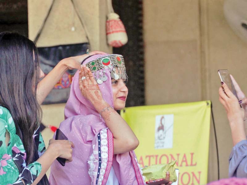 a girl tries out traditional jewellery while another takes her picture at the national exhibition of textiles at the lok virsa in islamabad photo online