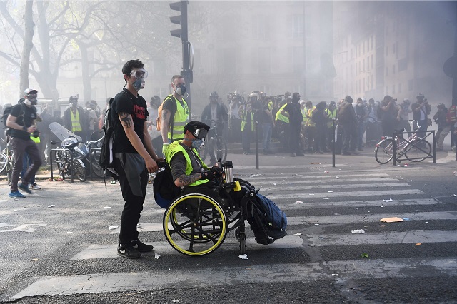 a protester in wheelchair sits amid tear gas during clashes with police on april 20 2019 in paris as thousands of quot yellow vest quot gilets jaunes protesters took to the streets a 23rd week of anti government marches photo afp