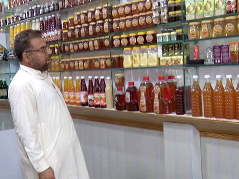 a customer looks at a large variety of honey bottles at a shop that also sells whole beehives in peshawar photos express