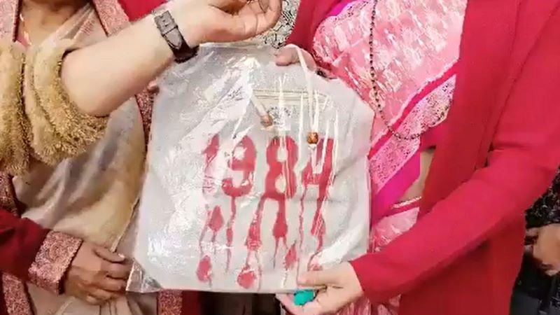 bjp lok sabha mp from odisha aparajita sarangi with a bag 1984 written on it in red and handed it over to congress mp priyanka gandhi photo the hindu