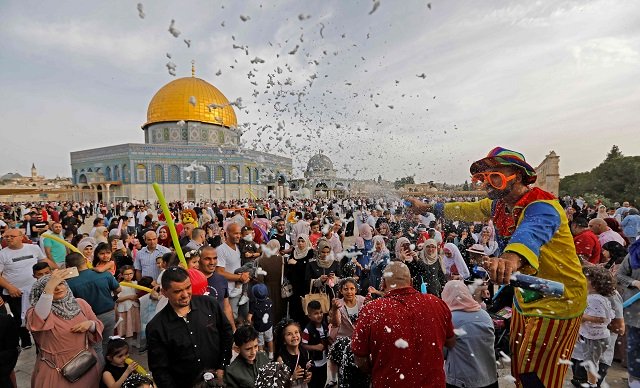 a clown entertains people as palestinian muslims perform the morning eidul fitr prayer near the dome of rock mosque at al aqsa mosque compound photo afp