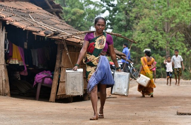 an indian woman carries water in stainless steel cans at shakar pada village near shahapur on the outskirts of mumba photo afp