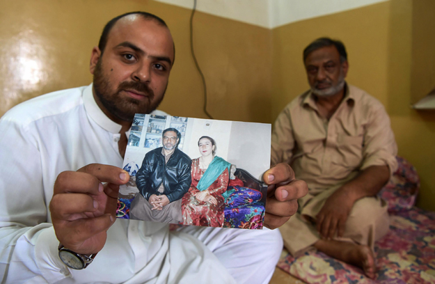 In this photograph Shehzada Khurram (L) along with his father Imtiaz Javed holds a picture of his mother Shabana Shaheen, who was killed by a stray bullet in 2015 when supporters of a winning candidate in local government polls started celebratory gunfire in Peshawar. PHOTO: AFP