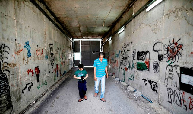 palestinian omar hajajla walks with his son through the tunnel connecting their home in jerusalem to al walajah their village in the occupied west bank on may 30 2019 photo afp