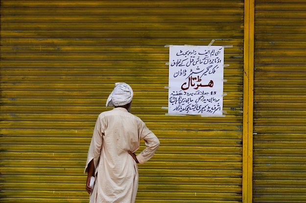 a worker reads a sign on a closed shop in peshawar during a shutter down strike called by the traders and business community against what they say is a harsh federal budget for the fiscal year 2019 20 the sign reads in urdu quot countrywide shutter down strike against the imf sponsored budget and economic murder of businessmen quot photo reuters