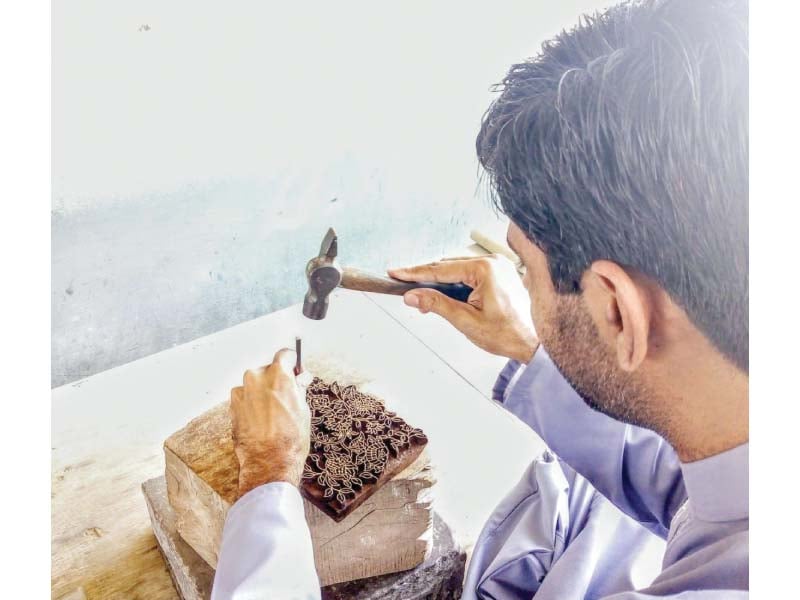 a craftsman does intricate work while carving out the design on the block which will later be printed on cloth photo express