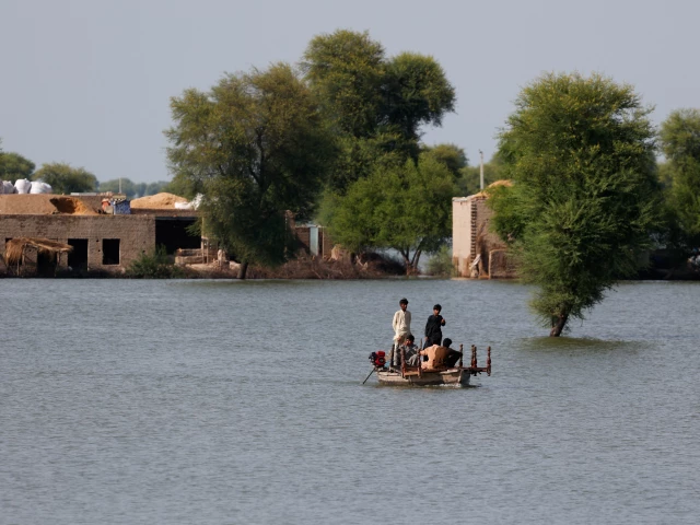 residents travel in boat with the partially submerged homes in the background following monsoon rains and rising water levels of indus river on the outskirts of dadu sindh reuters akhtar soomro