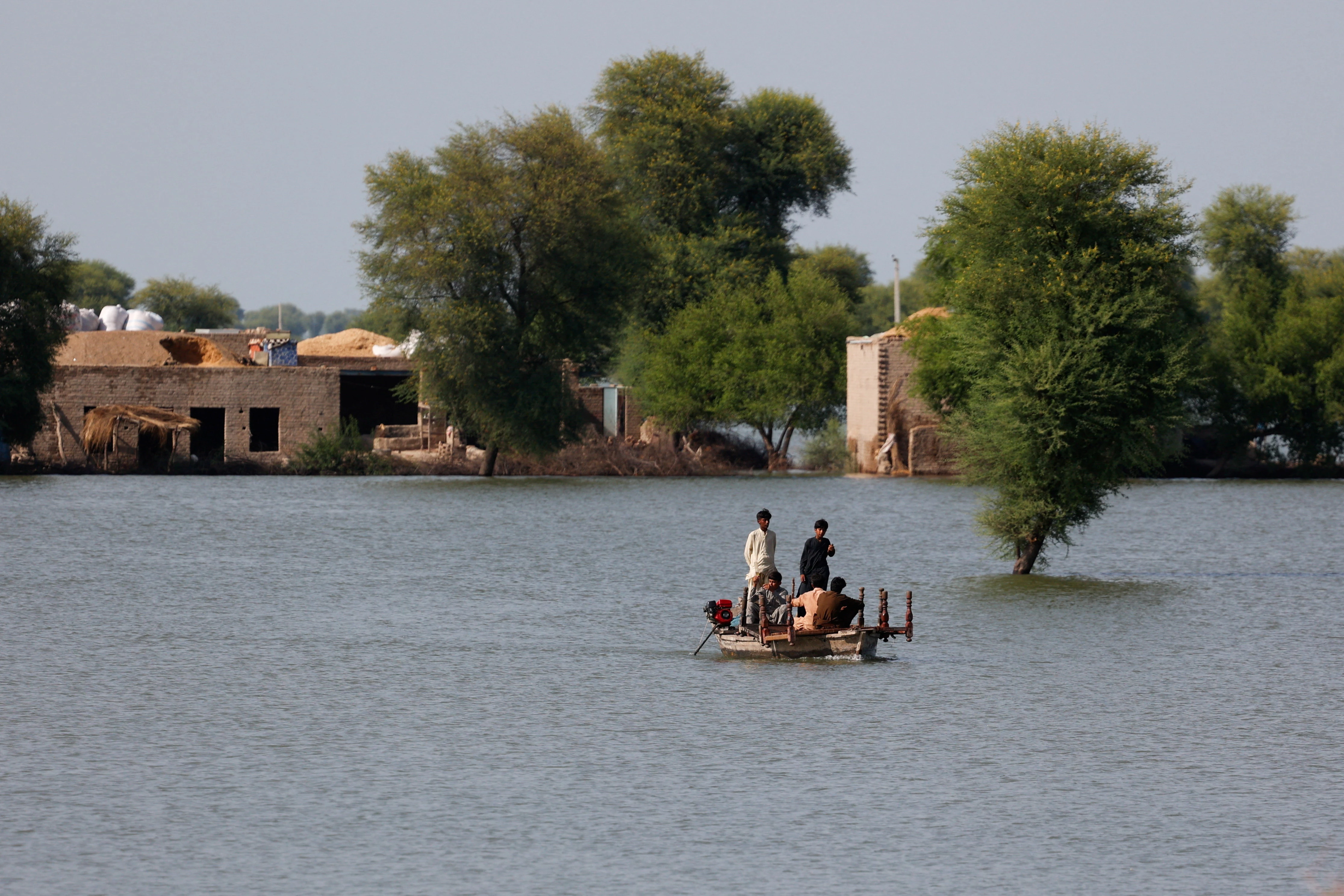 residents travel in boat with the partially submerged homes in the background following monsoon rains and rising water levels of indus river on the outskirts of dadu sindh reuters akhtar soomro