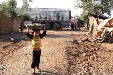 a child walks carrying a basin over the head on a footpath by a field at a camp for displaced syrians near the village of shamarin near the border with turkey in the northern syrian aleppo province photo afp