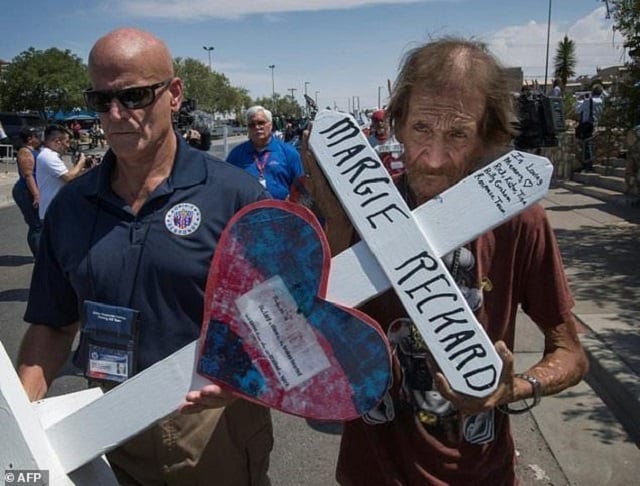 antonio basco right holds the cross of his common law wife margie reckard who died in the el paso shooting as he walks to a makeshift memorial photo afp