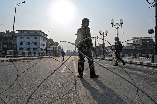 indian paramilitary troopers stand guard behind a barbed fence wire as they block a road during a curfew in srinagar photo afp
