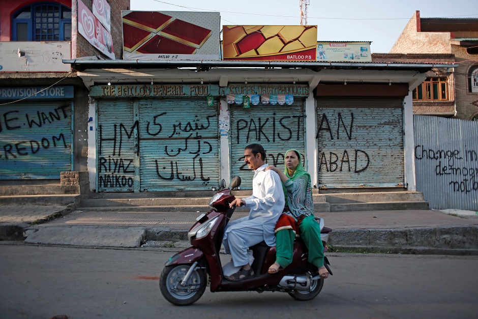 kashmiris ride on a scooter past the closed shops painted with graffiti during restrictions after scrapping of the special constitutional status for kashmir by the indian government in srinagar photo reuters