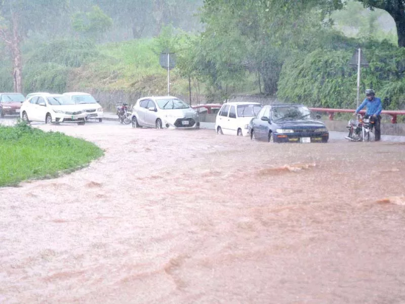 commuters tread through rainwater on a road in islamabad photo app
