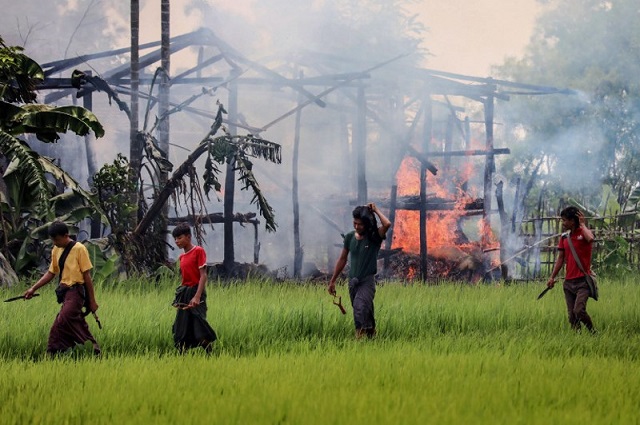 unidentified men carry knives and slingshots as they walk past a burning house in gawdu tharya village near maungdaw in rakhine state in northern myanmar on september 7 2017 photo afp