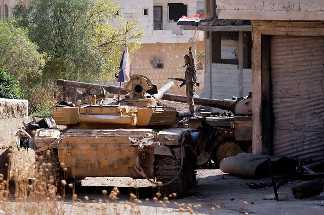 a syrian army soldier holds a syrian flag as he stands on a military vehicle in khan sheikhoun idlib syria august 24 2019 photo reuters