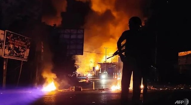 an armed indonesian policeman stands guard near a burning building after hundreds of demonstrators marched near papua 039 s biggest city jayapura on aug 29 2019 where they set fire to a regional assembly building and hurled rocks at shops and hotels photo afp