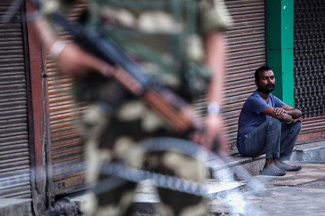 a security personnel stands guard as a man sits in front of a closed shop in jammu on august 6 2019 photo afp