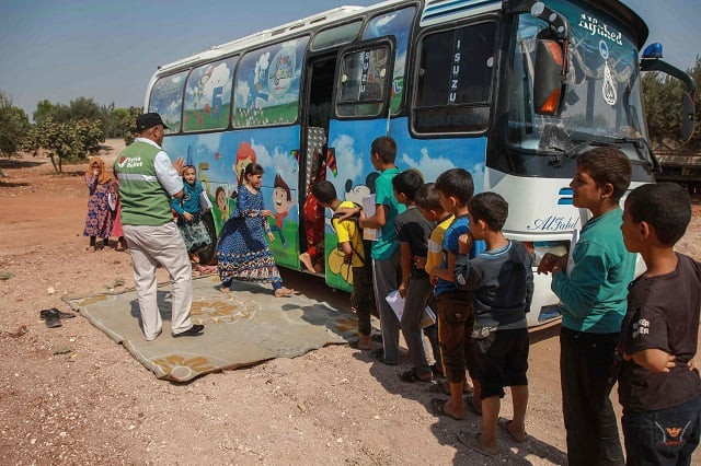 displaced syrian children queue for their turn outside a bus converted into a classroom in the village of hazano in northwestern syria on september 15 2019 the buses cater only for ages ranging from 5 to 12 and include classes in arabic mathematics science and sometimes english as well as singing and drawing photo afp