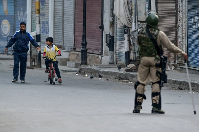 a security personel stands guard as a kashmiri child on a bicycle passes by along with a man during a lockdown at amira kadal in srinagar on september 27 2019 photo afp a security personel stands guard as a kashmiri child on a bicycle passes by along with a man during a lockdown at amira kadal in srinagar on september 27 2019 photo afp