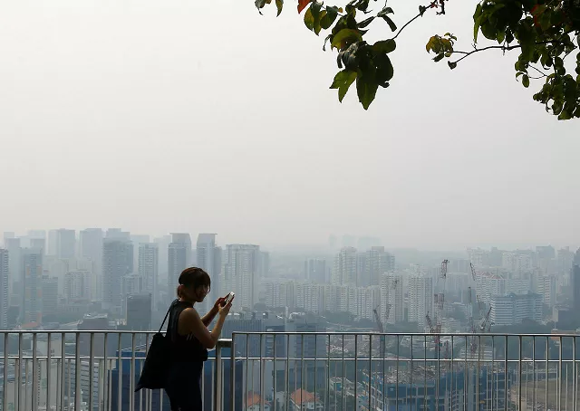 a woman uses her phone on an observation deck as the skyline shrouded by haze is seen in singapore september 13 2019 photo reuters a woman uses her phone on an observation deck as the skyline shrouded by haze is seen in singapore september 13 2019 photo reuters