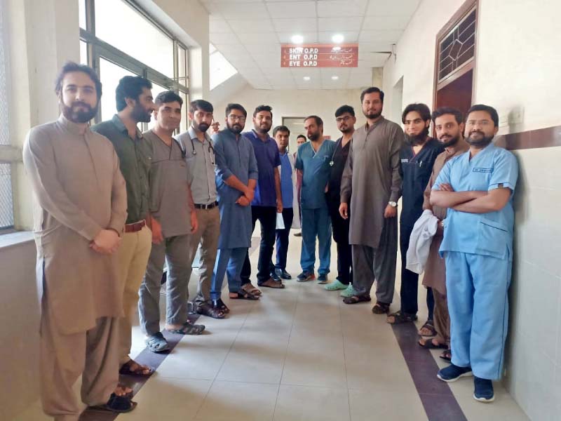 protesting doctors pose for a group photo while a distraught woman sits next to her relative lying on a stretcher outside the closed opd of bbh hospital in rawalpindi on friday photos express nni